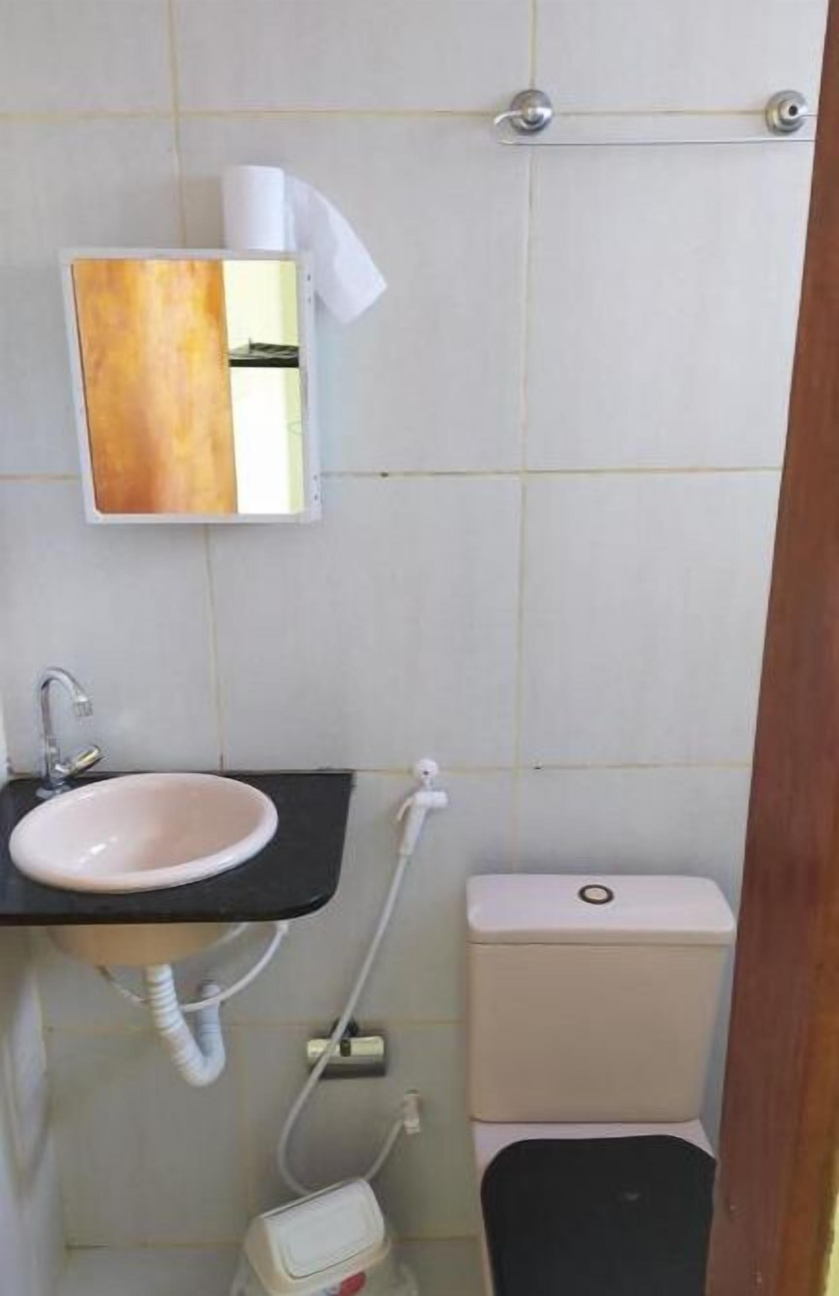 Uma casa de banho com uma pia branca, um espelho, uma sanita e um dispensador de toalhas.