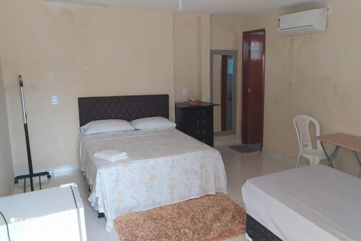 A hotel room with two beds, a desk, a chair, a wardrobe, and an air conditioning unit.