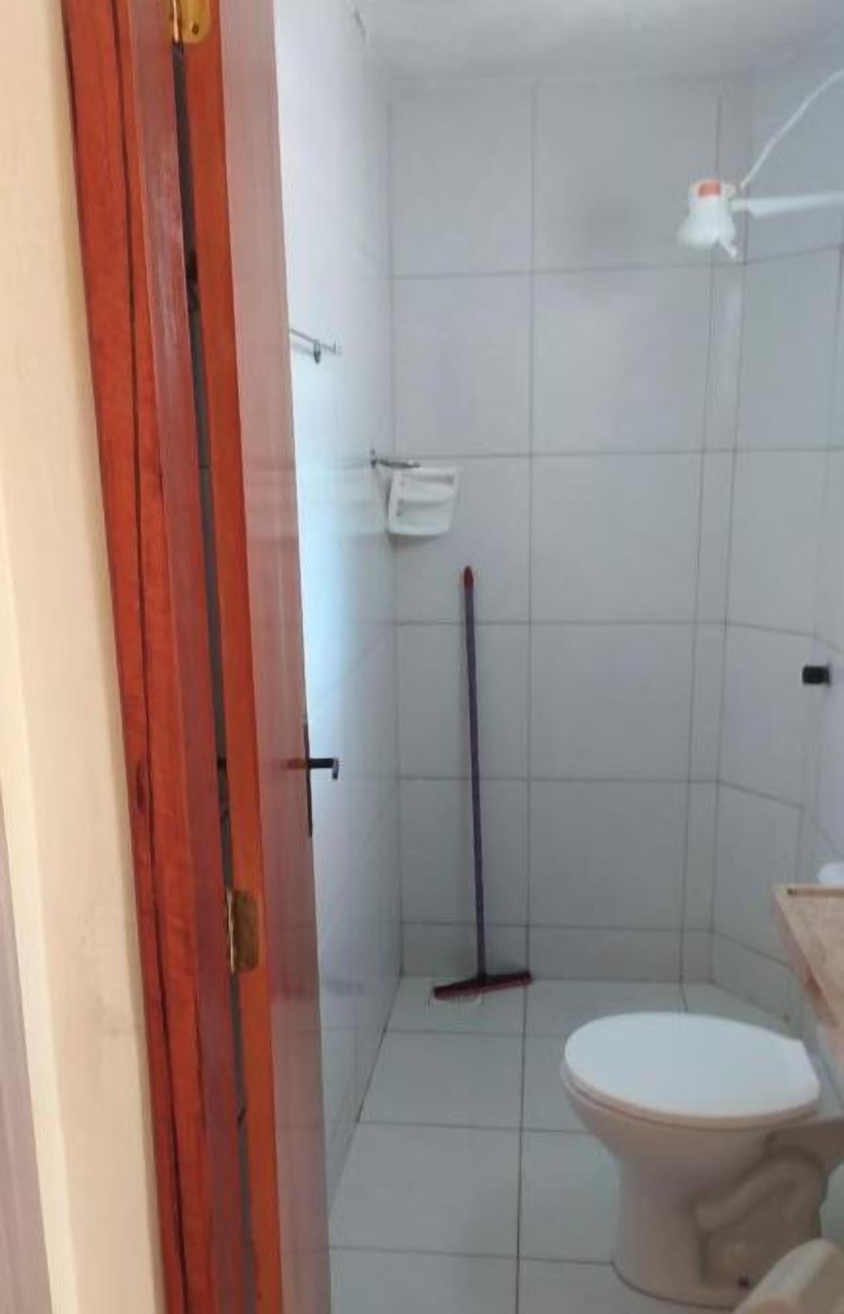 Un baño con inodoro, ducha y un trapeador apoyado en la pared.