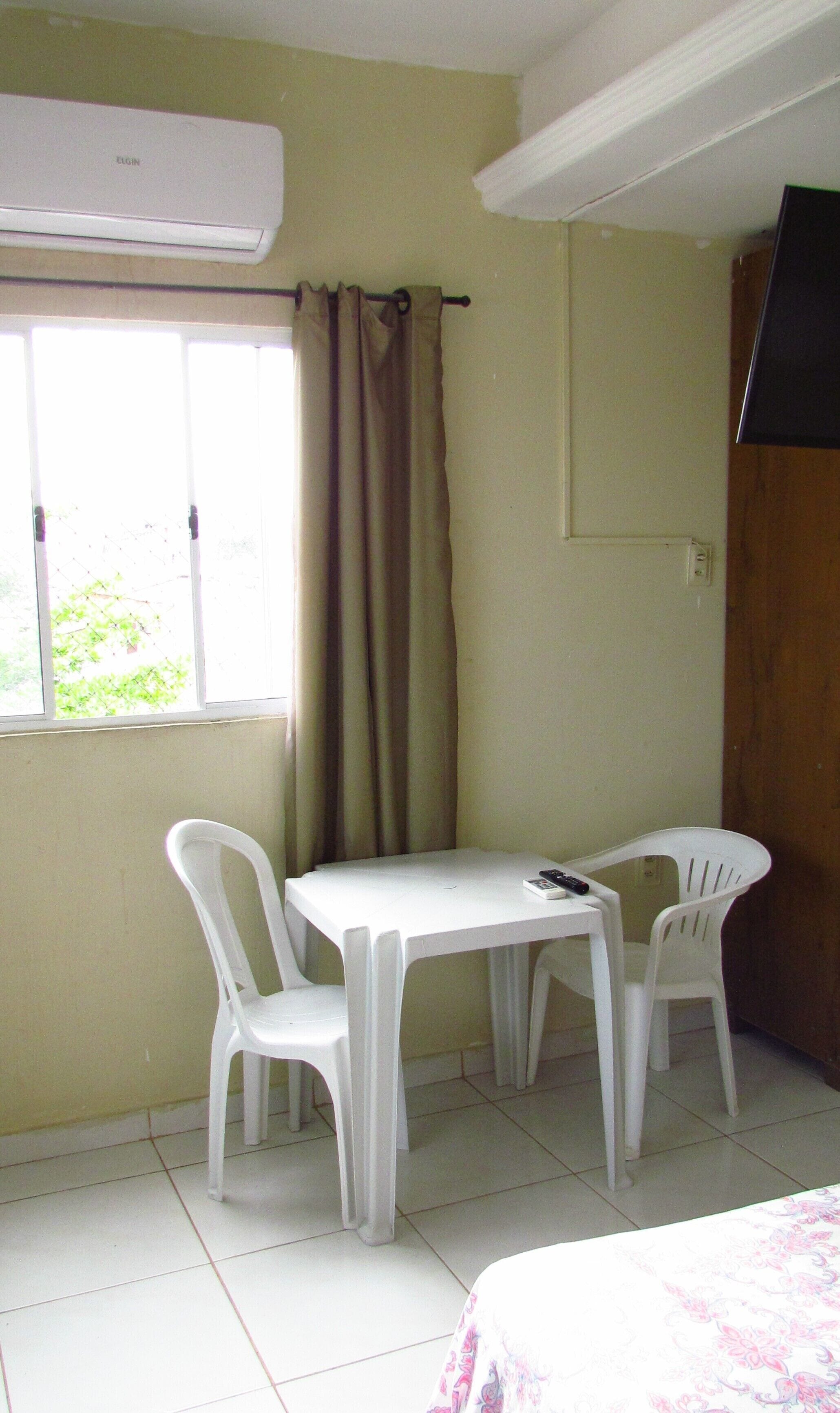 A small room with a window, a table with two chairs, and a bed.