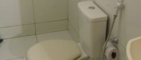 A small, basic bathroom with a toilet, a sink, and a toilet paper holder.