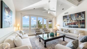 A spacious living room with a large window, a ceiling fan, and a view of the ocean.