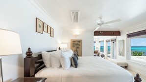 Ein geräumiges Schlafzimmer mit einem großen Bett, einem Nachttisch, einem Deckenventilator und Meerblick durch große Fenster.