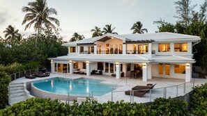 Una casa de dos pisos con piscina, mobiliario exterior y un porche cubierto.