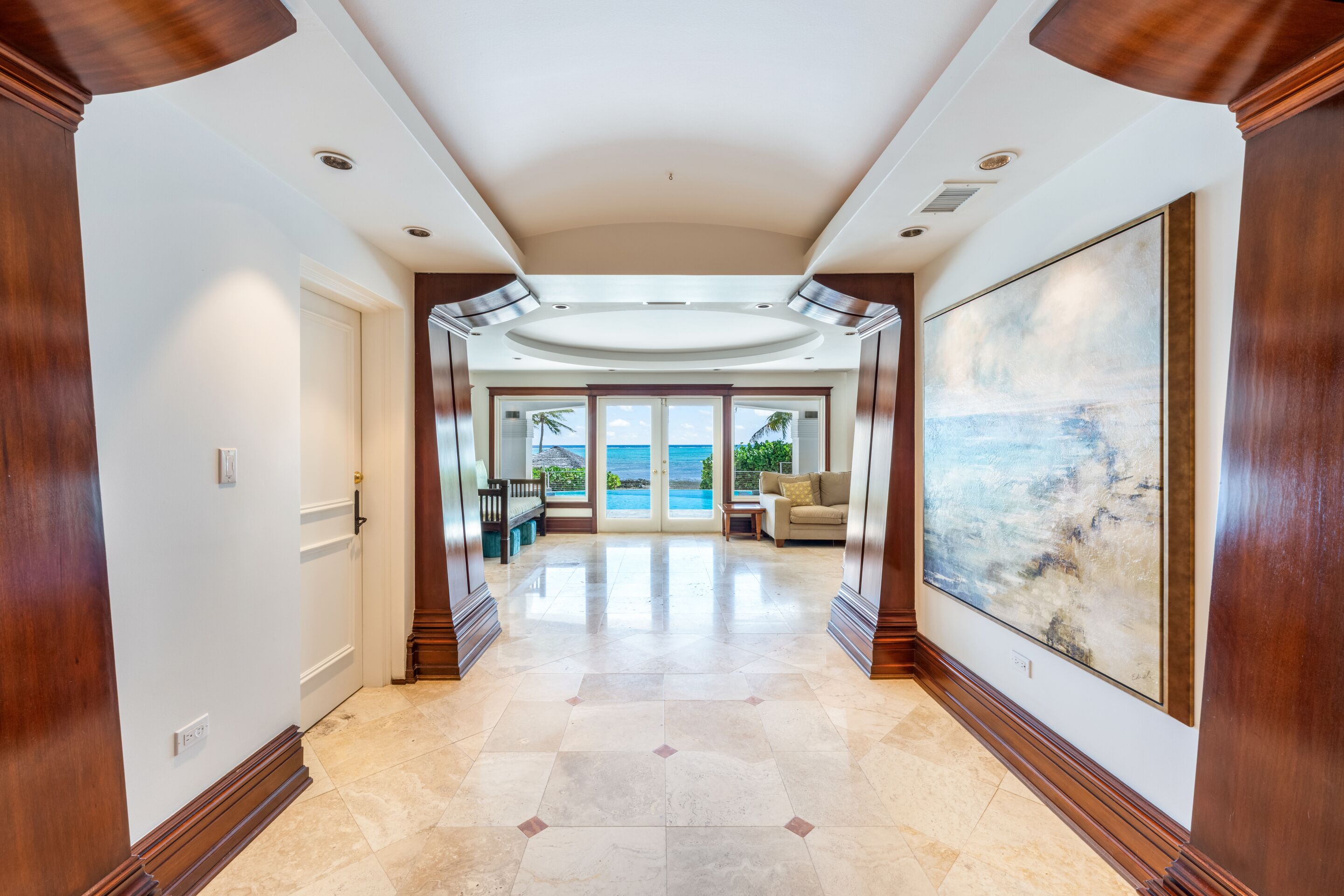 A spacious hallway with a view of the ocean, leading to a seating area with a large painting.