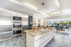 A modern kitchen with built-in ovens, a marble countertop, and a dining area with a view. - Pease Bay House Cayman Islands (Grand Cayman)