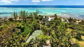 Una cancha de tenis rodeada de vegetación tropical exuberante y una playa con aguas turquesas cristalinas.