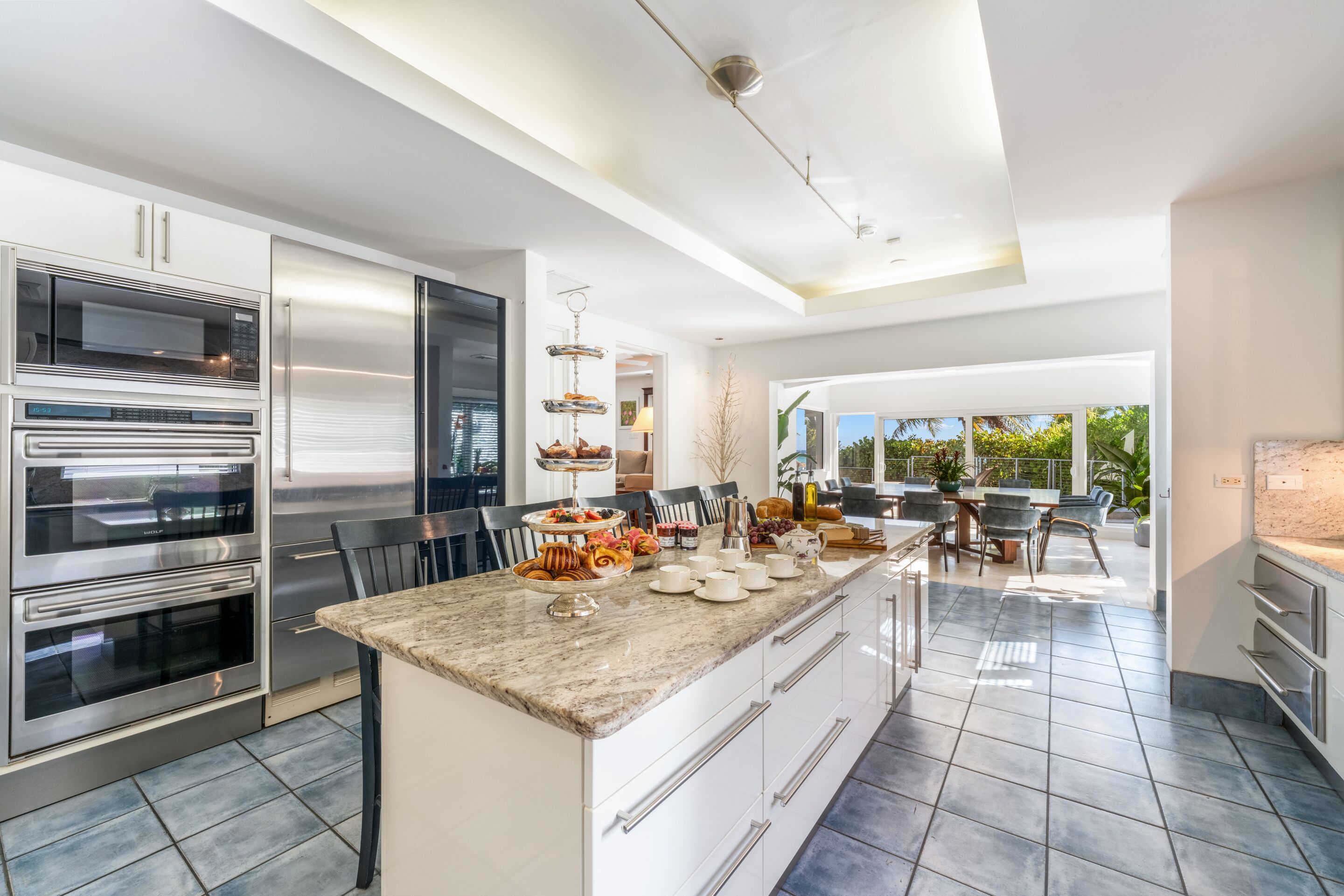 A modern kitchen with stainless steel appliances, a marble countertop, and a view to the outdoors.