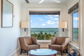 Una habitación con dos sillones a rayas, una mesa redonda de cristal y vistas al océano a través de amplios ventanales.