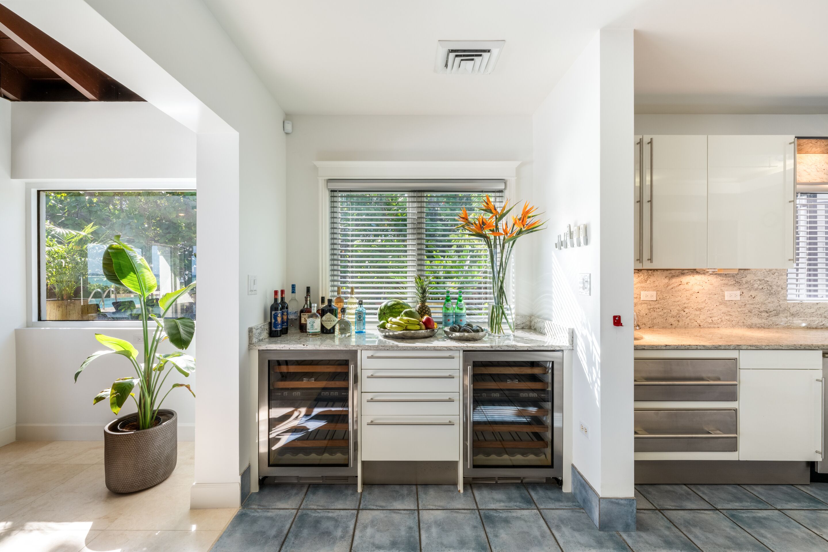 A modern kitchen with white cabinets, a built-in oven, and a window with blinds.