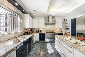 A modern kitchen with a central island, stainless steel appliances, and a marble backsplash. - Pease Bay House Cayman Islands (Grand Cayman)