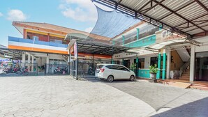 A parking area with a white car, a covered walkway, and a building with a tiled roof and colorful walls.