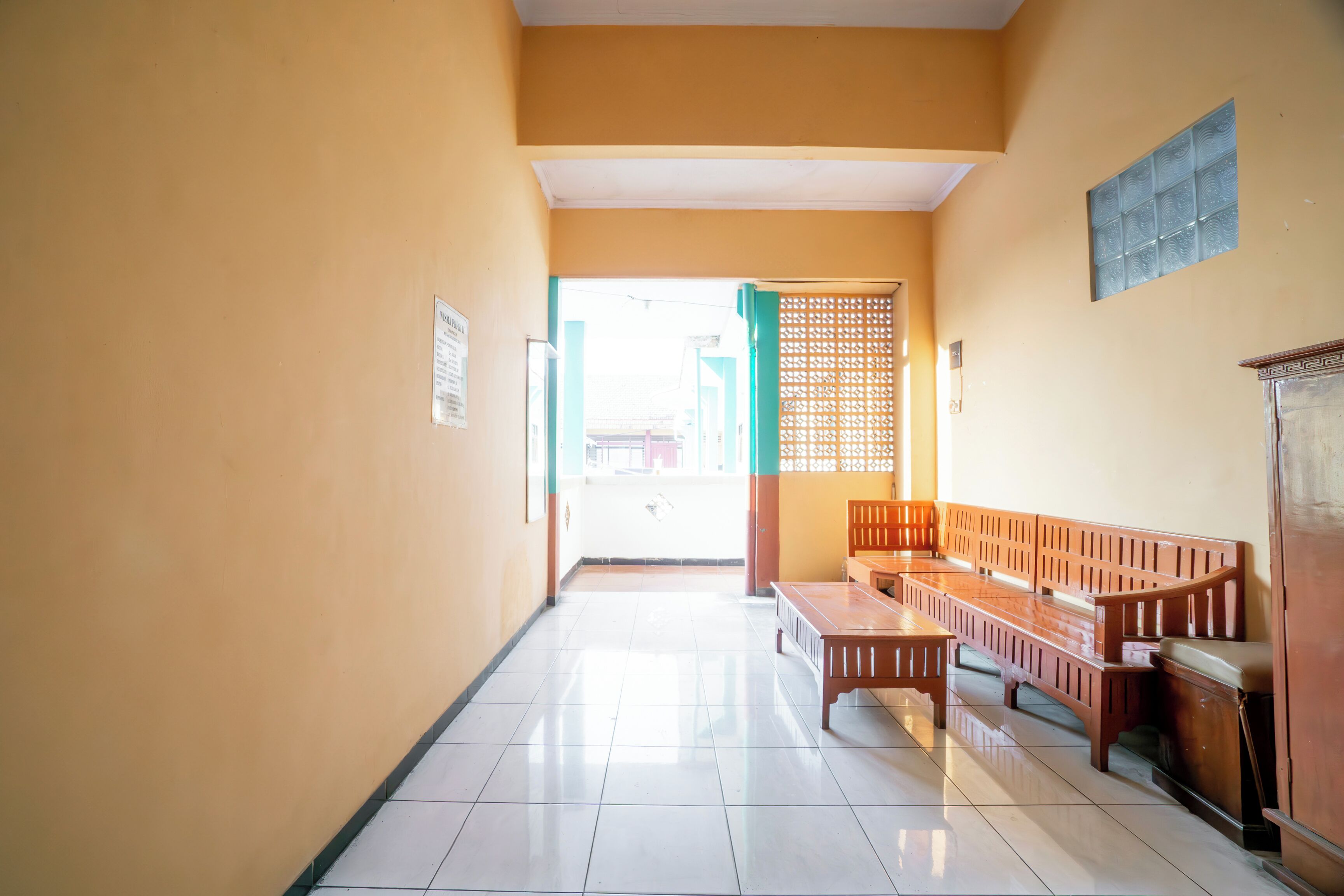 A hallway with a bench and a table, a door with a green frame, and a tiled floor.