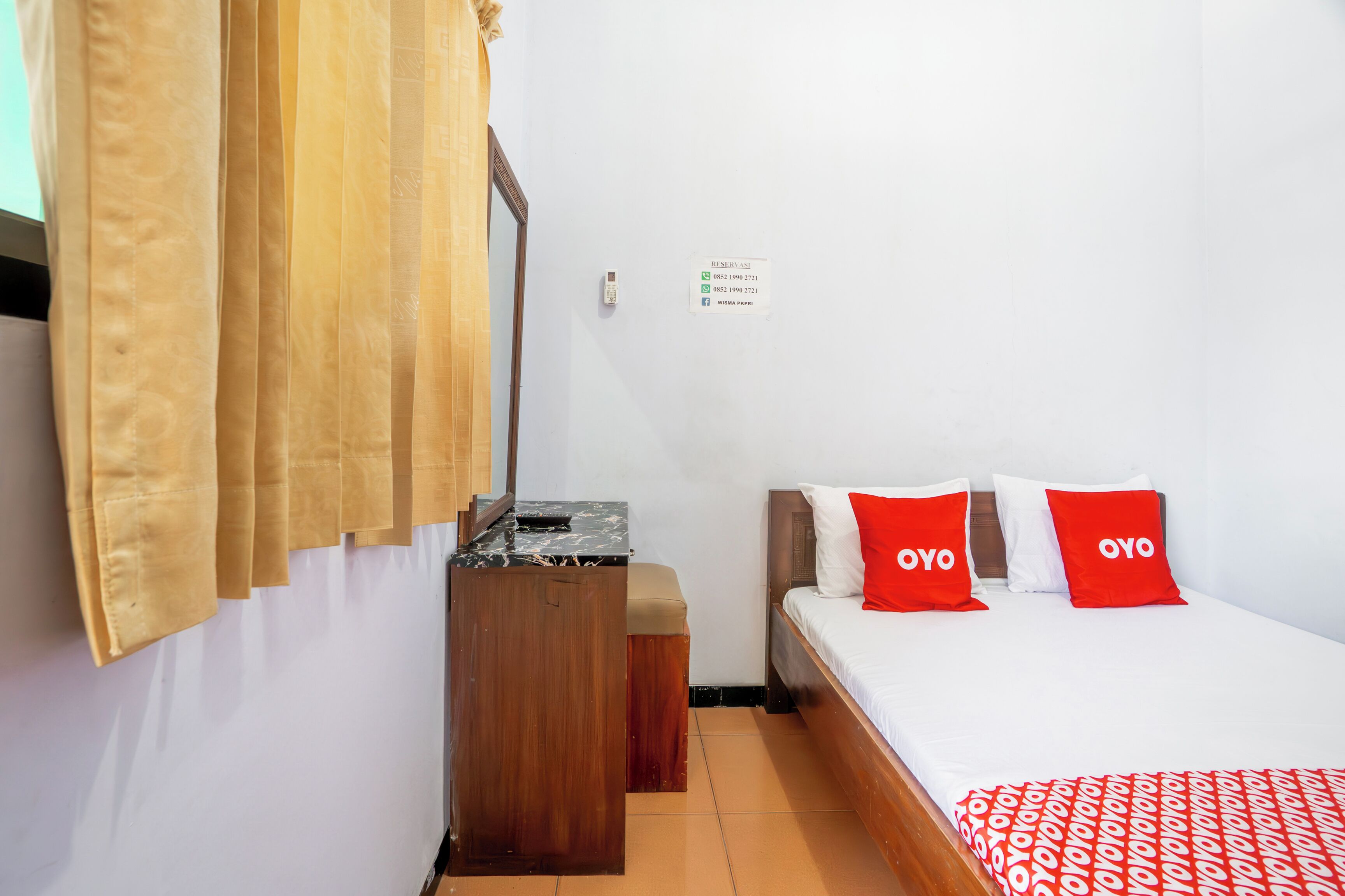 A hotel room with a bed, a wooden nightstand, a mirror, and a window with curtains.