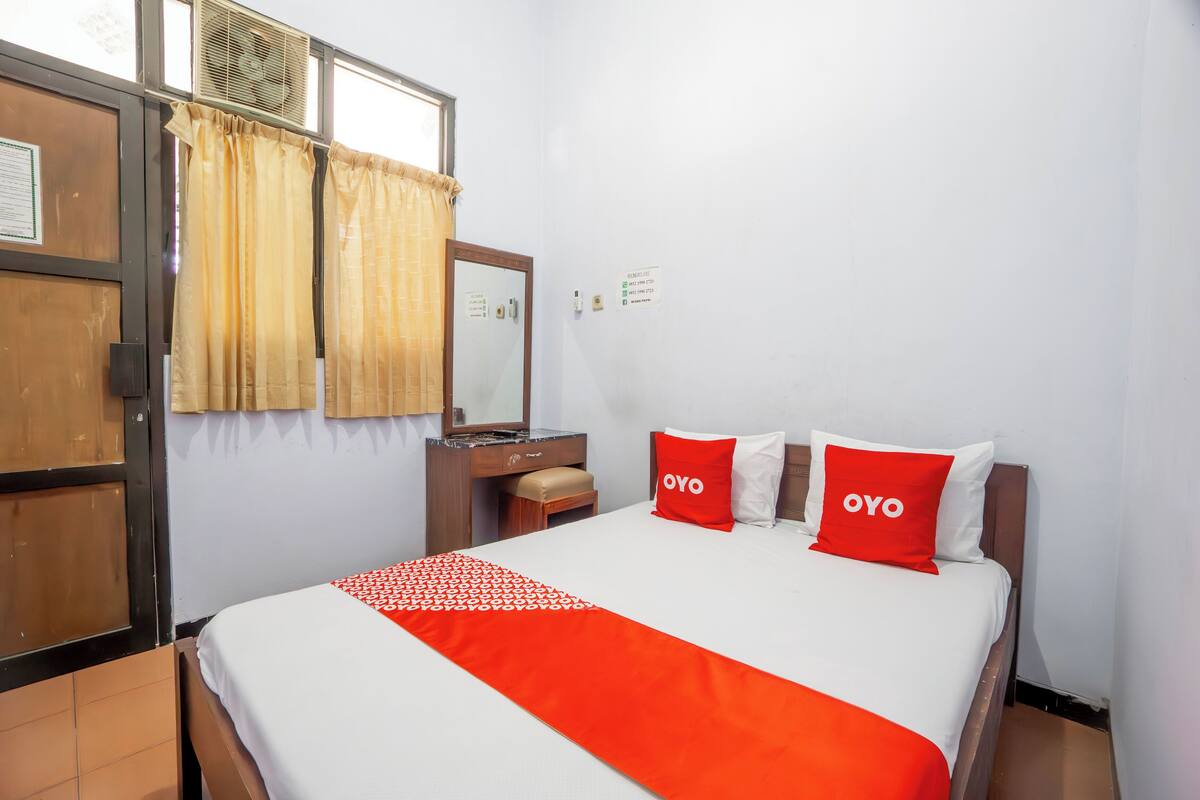 A hotel room with a bed, a nightstand, a mirror, and a window with curtains.