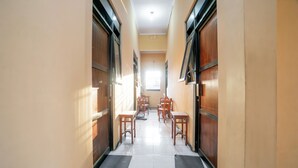 A hallway with wooden doors, tiled flooring, and several wooden tables and chairs arranged in the distance.
