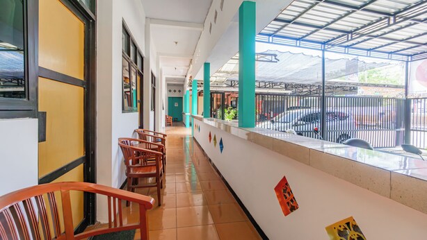 A corridor with wooden chairs, a tiled floor, and a view of a parking area through a glass fence.
