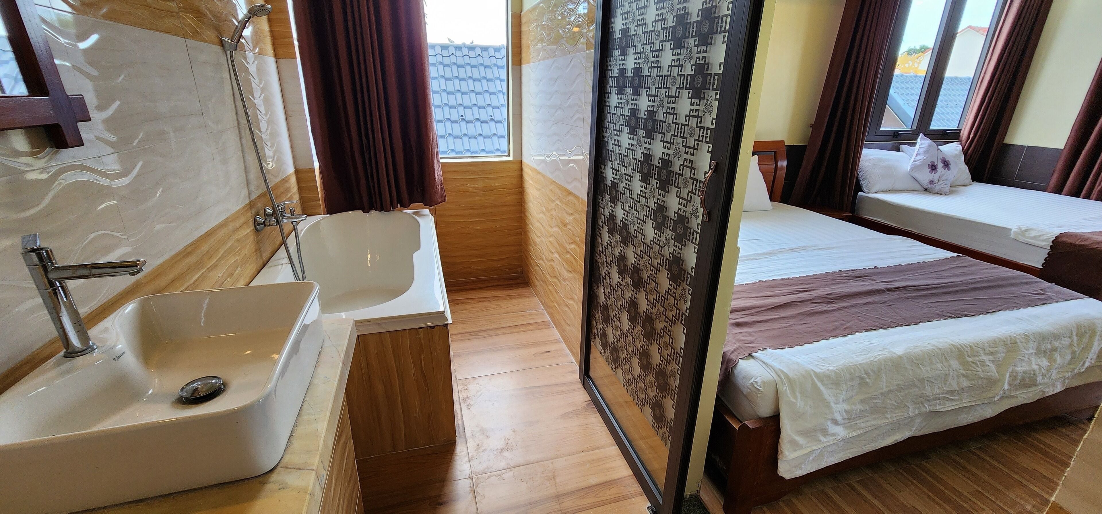 A hotel room with a bathtub, a sink, a window with curtains, and a bed with a white bedspread.