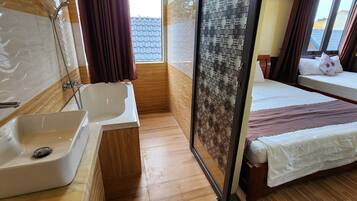 A hotel room with a bathtub, a sink, a window with curtains, and a bed with a white bedspread.