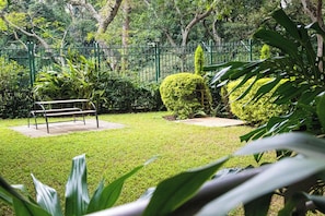 A well-maintained garden with a bench, neatly trimmed hedges, and a green fence.