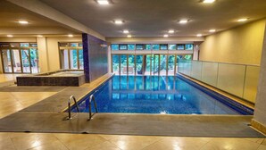 An indoor swimming pool with clear glass walls, a tiled floor, and a view of greenery outside. - Lion Villas (Nairobi)