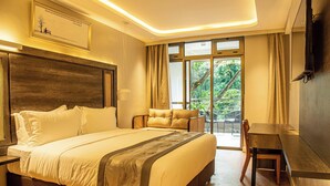 A hotel room with a large bed, a desk, and a balcony with a view of greenery. - Lion Villas (Nairobi)