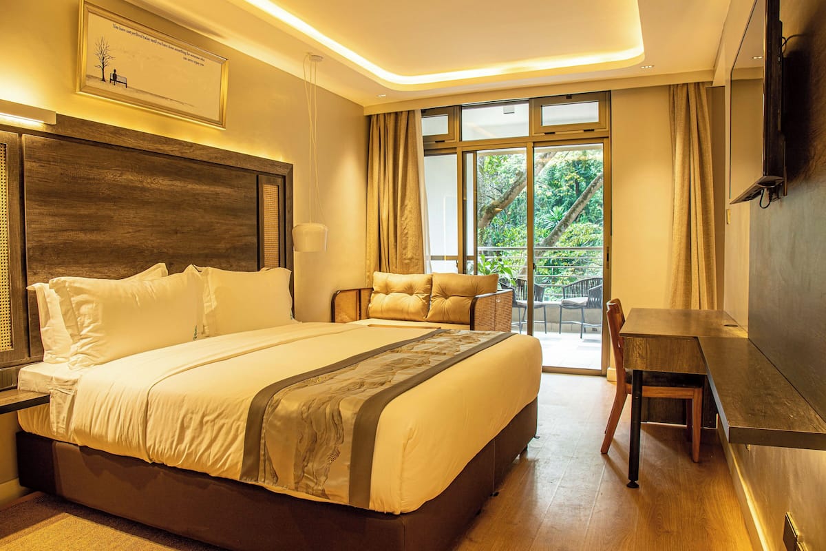 A hotel room with a large bed, a desk, and a balcony with a view of greenery.