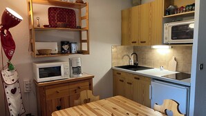 Una cocina compacta con armarios de madera, un microondas, una cafetera y un lavabo.