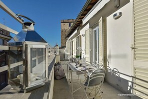 Un balcon étroit avec une table et des chaises, un télescope, et une vue sur un bâtiment historique en arrière-plan.