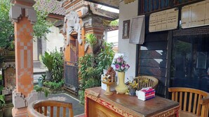 An outdoor seating area with wooden chairs and a table, surrounded by plants and traditional architecture. - Super OYO Capital O  Pondok Ayu Homestay (Ubud)