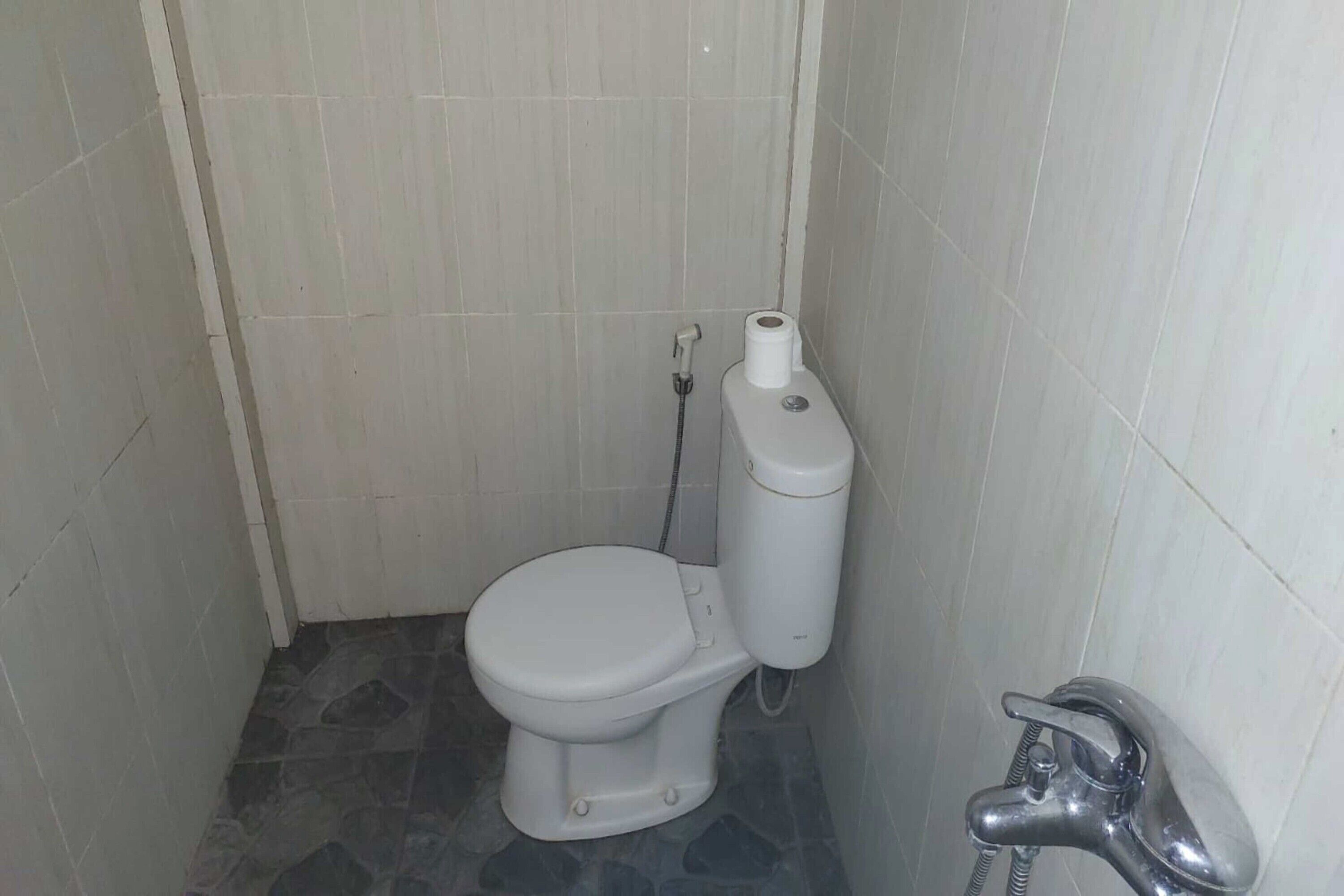 A small, compact bathroom with a white toilet, a visible toilet paper holder, and a shower faucet.