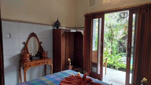 A hotel room with a bed, a wooden dresser, a mirror, and a view of a garden through a glass door. - Super OYO Capital O  Pondok Ayu Homestay (Ubud)