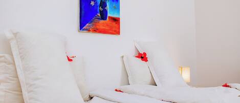 Habitación de hotel con dos camas, ropa de cama blanca y un cuadro de un jarrón azul con flores en la pared.
