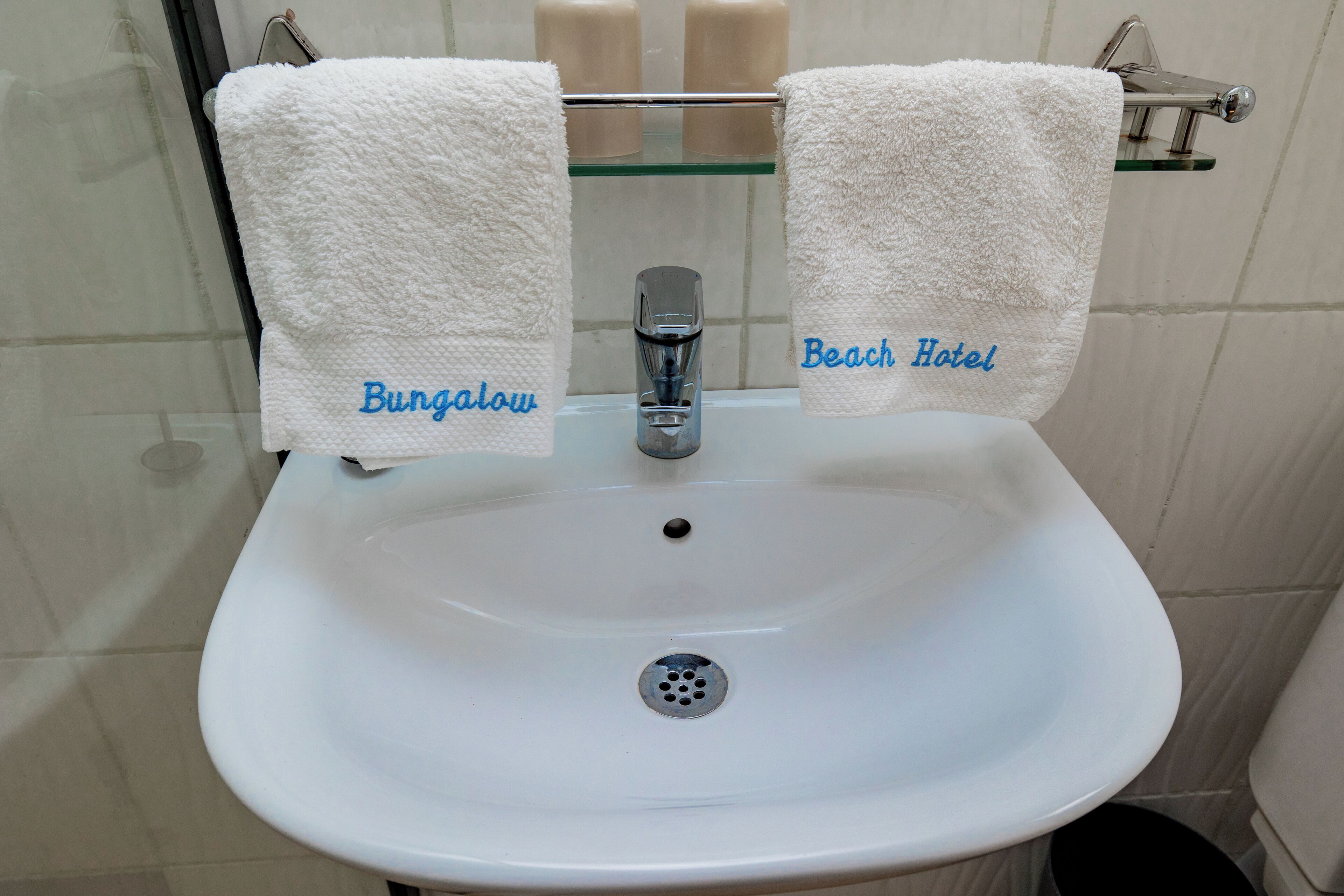 A bathroom sink with two white towels hanging on a rack, labeled "Bungalow" and "Beach Hotel."