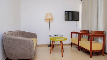 Una habitación con un sillón gris, una mesa amarilla y dos sillas de madera.