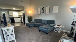 A living room with a sectional sofa, a small white table, and a grey carpet. - NEW - Minimalistic Farmhouse! (Jacksonville)