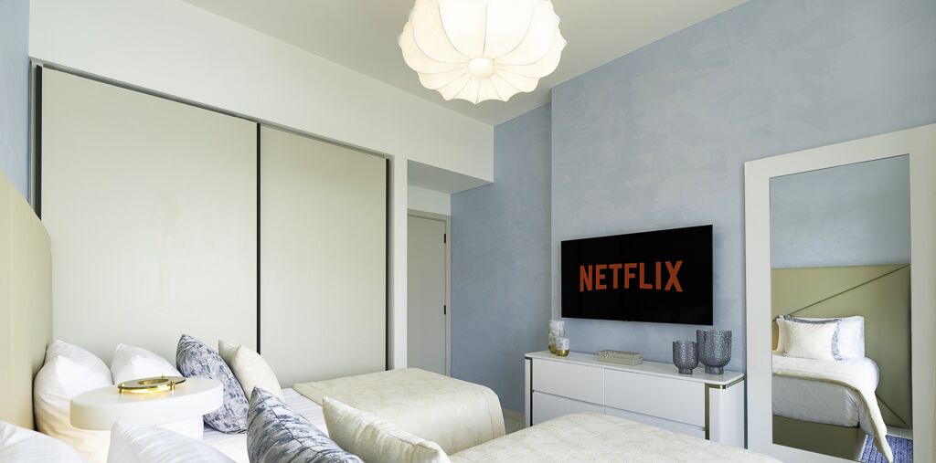 A modern bedroom with a large bed, a bedside table, a TV mounted on the wall, and a wardrobe.