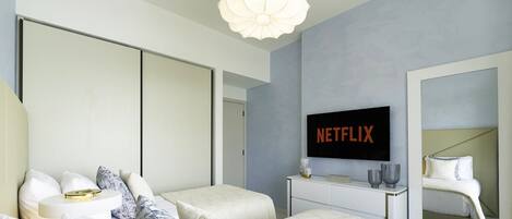 A modern bedroom with a large bed, a bedside table, a TV mounted on the wall, and a wardrobe.
