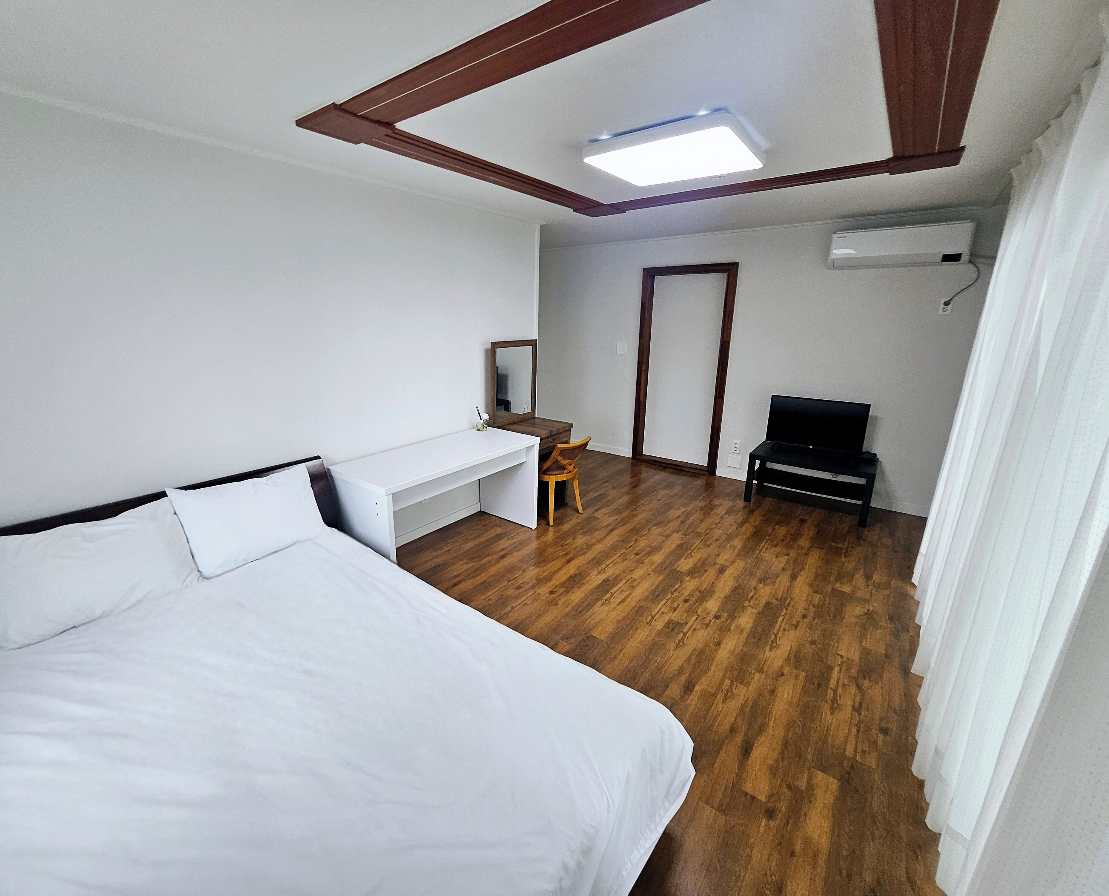 A hotel room with a bed, a desk, a chair, a television, and an air conditioning unit.