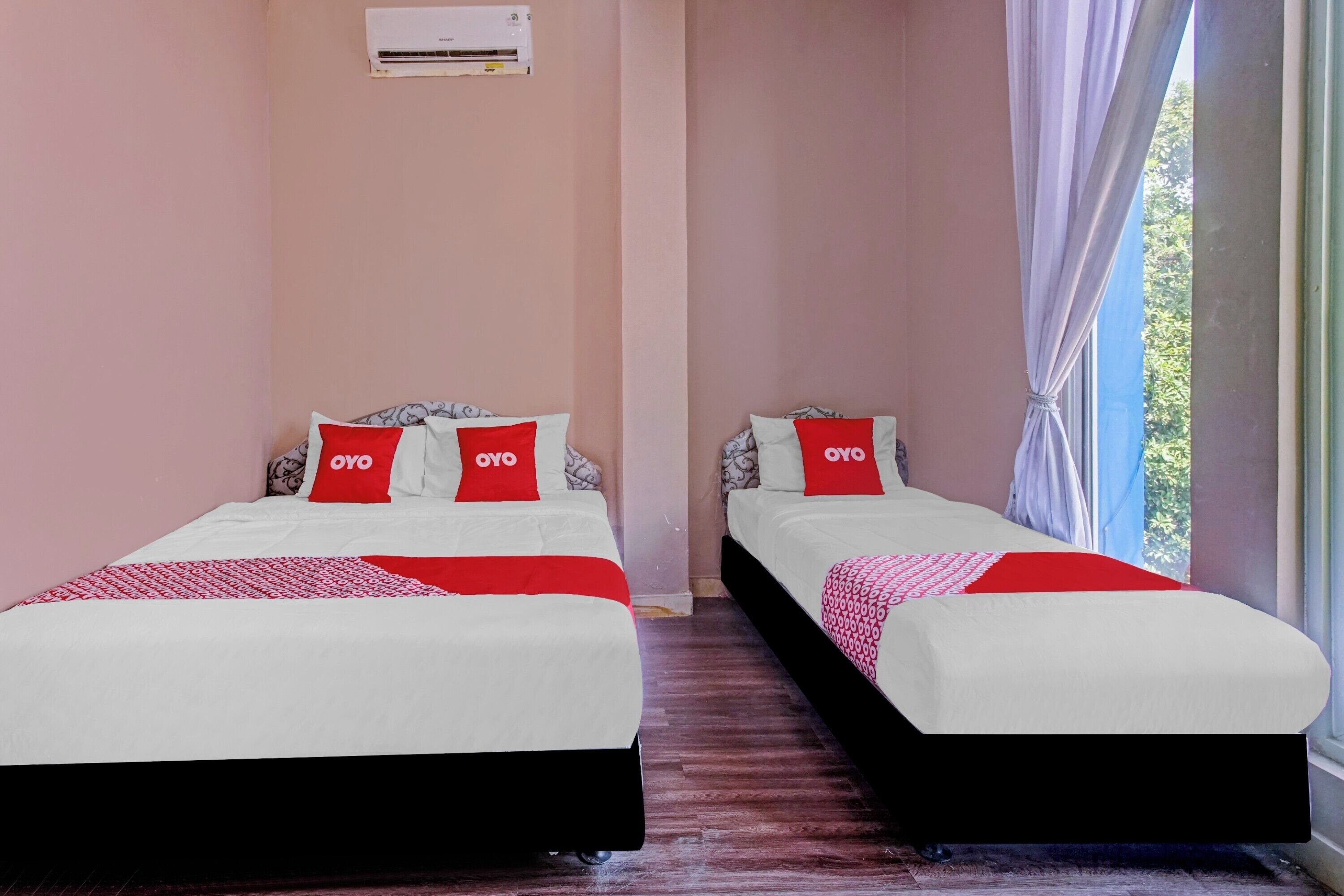 Two beds with red and white bedding, a window with curtains, and an air conditioning unit on the wall.