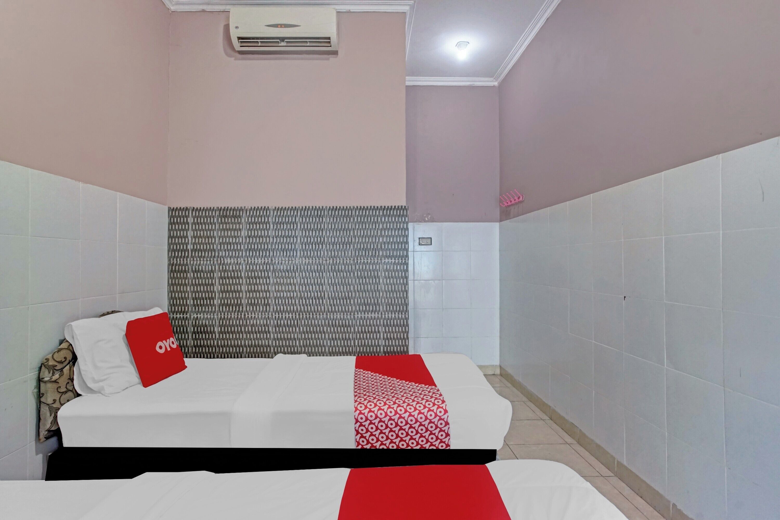 A hotel room with two beds, a patterned headboard, and a tiled wall.