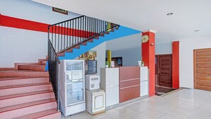 Un escalier avec des marches rouges menant à un palier, un réfrigérateur, un distributeur d’eau et une horloge au mur.
