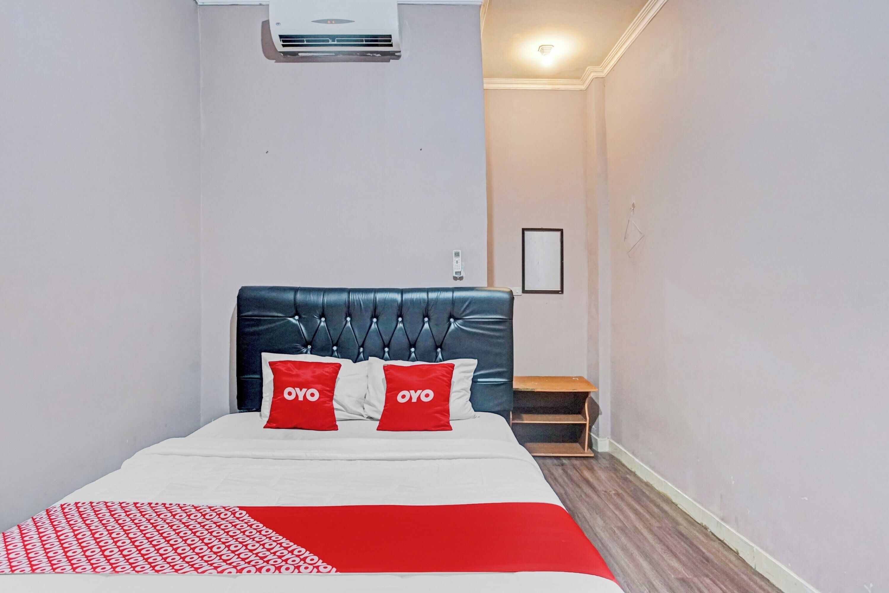 A hotel room with a bed, a headboard, a bedside table, and a wall-mounted air conditioner.