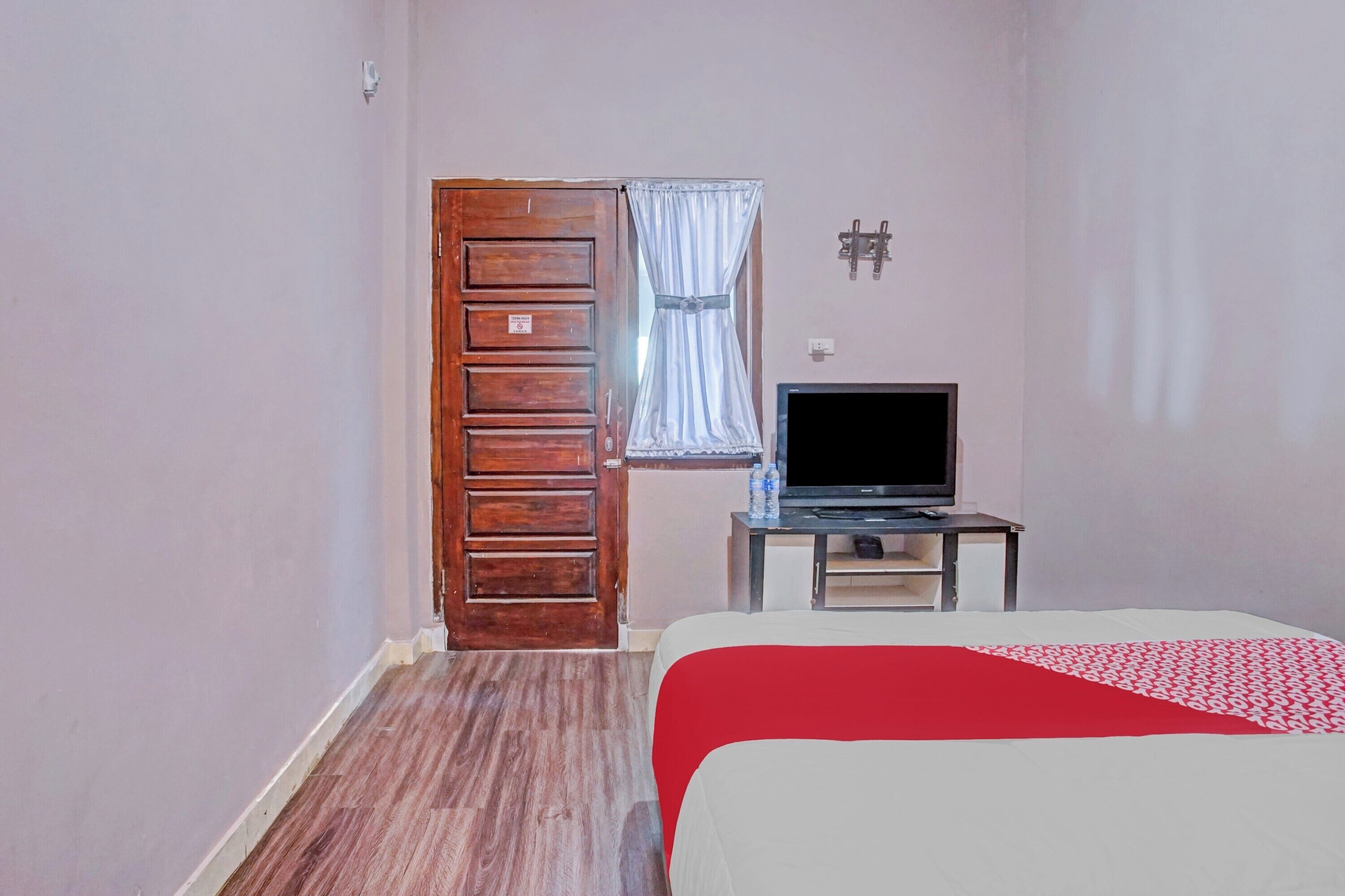 Ein Schlafzimmer mit Holztür, einem Fernseher auf einem kleinen Tisch und einem Bett mit rotem und weißem Überwurf.