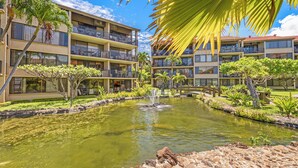 A hotel with multiple balconies, a central pond with a fountain, and tropical landscaping.
