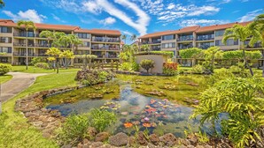 A hotel with a central pond surrounded by lush greenery and a clear blue sky.