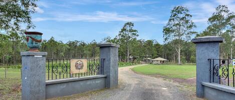 A gated entrance with a decorative urn, a signboard, and a gravel path leading to a building.