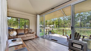 Une pièce comprenant un canapé, une table avec un globe terrestre et un carnet, un téléviseur, et une porte-fenêtre coulissante donnant sur une terrasse extérieure avec des chaises et une table.