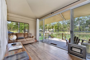 Une pièce comprenant un canapé, une table avec un globe terrestre et un carnet, un téléviseur, et une porte-fenêtre coulissante donnant sur une terrasse extérieure avec des chaises et une table.
