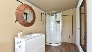 Une salle de bain avec un lavabo blanc, un miroir rond et une cabine de douche en verre.